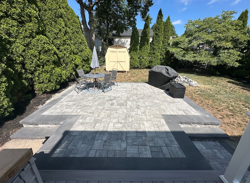 Completed multi-level backyard paver patio with charcoal border and outdoor dining area in Northern New Jersey